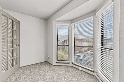 A room with a carpeted floor, a window with blinds, and a door with a window.at Rock 35, Round Rock