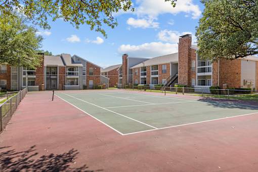 A tennis court is surrounded by a brick building.