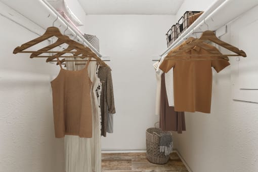 a walk in closet in a bedroom with white walls and a white wardrobe with wooden hangers  at Vesper, Dallas, TX, 75254