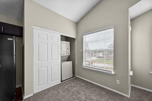 A room with a white door, a window with blinds, and a black refrigerator.