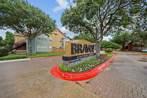 A sign for Bravo Apartments is in front of some trees and buildings.