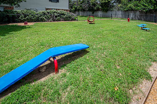 A blue seesaw in a grassy playground area.