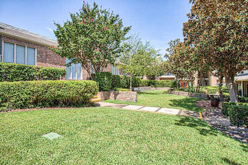 A well-maintained lawn with a tree and a house in the background.