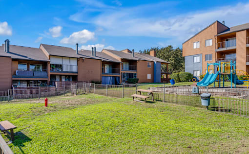 A playground with a slide and a fire hydrant is in front of apartment buildings.