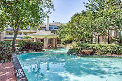 A pool surrounded by trees and bushes with a house in the background.
