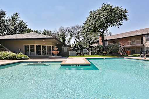 A swimming pool in front of a building with a tree in the background.