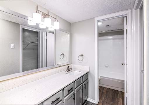 A bathroom with a white counter top and a mirror above it.