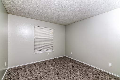 A room with a carpeted floor and a window with blinds.