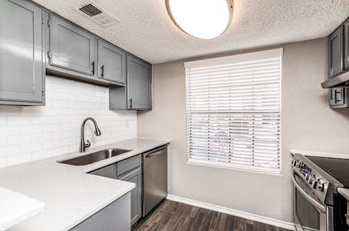 A kitchen with a white counter top and a stainless steel sink.