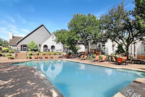 A swimming pool surrounded by chairs and trees.