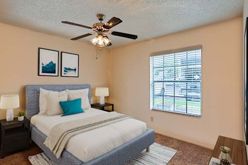 A bedroom with a bed, two lamps, a ceiling fan, and two pictures on the wall.