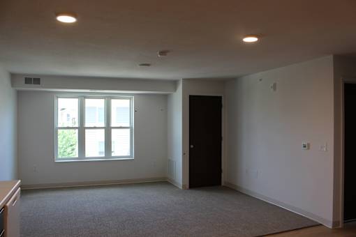 A large empty room with a window and carpeted floor.