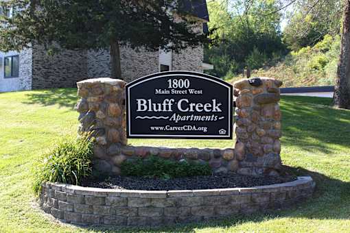 A sign for Bluff Creek Apartments is displayed in front of a building.