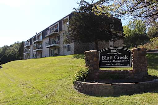 A sign for Bluff Creek Apartments stands in front of a building.