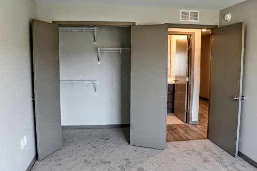 A bedroom with a closet and bathroom in the background on the other side of the hallway