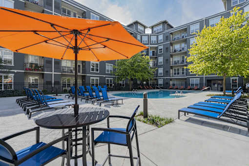 A large orange umbrella is in the middle of a poolside table and chairs.