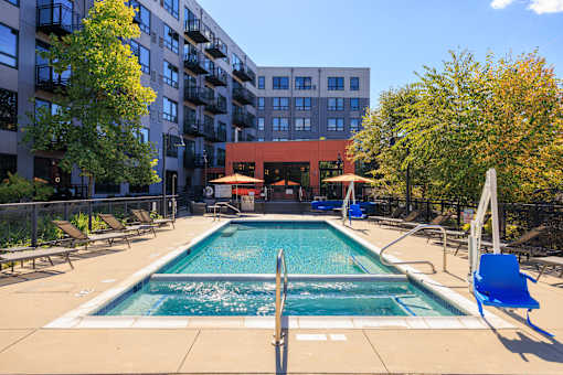 A swimming pool surrounded by chairs and trees in front of a building.