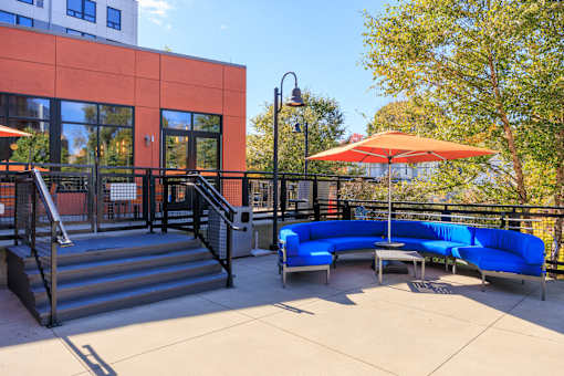 A blue couch is on a patio with a red umbrella.