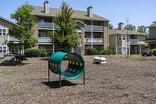 A green playground slide in front of apartment buildings.