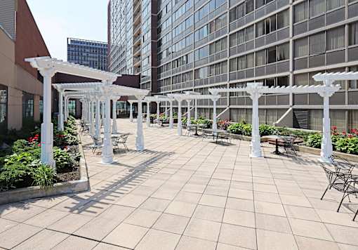 A patio with white pergolas and chairs is surrounded by buildings.