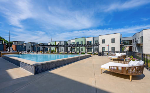 A pool area with a sun lounger and a building in the background.