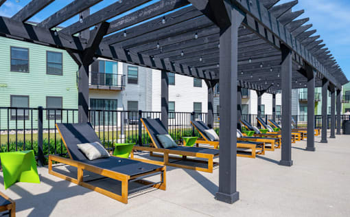 A row of sun loungers are arranged under a wooden pergola.