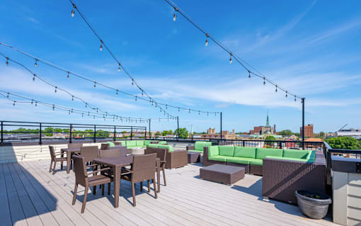 A rooftop patio with wooden flooring, tables and chairs, and string lights.