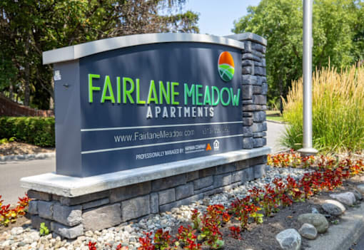 A sign for Fairlane Meadow Apartments is displayed in front of a landscaped area.