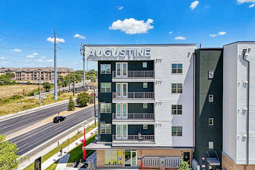 A street view of a building named Augustine with a car passing by.