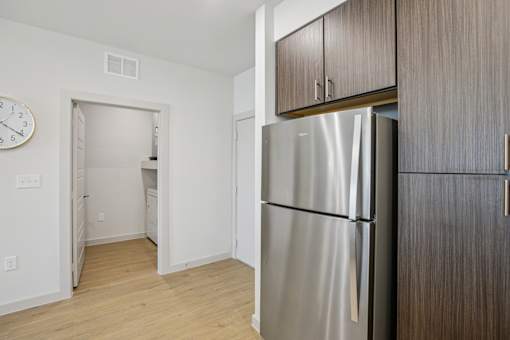 A kitchen with a refrigerator and wooden cabinets. at ThreeTwenty at the Vybe Apartments, Kyle, TX