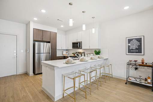 A modern kitchen with a white island and gold bar stools. at ThreeTwenty at the Vybe Apartments, Kyle, Texas