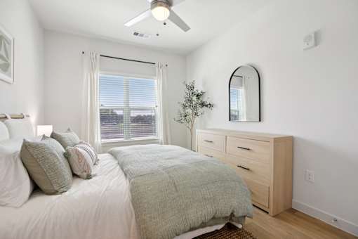A bedroom with a bed, dresser, mirror, and window. at Park South Apartments, Texas, 78748