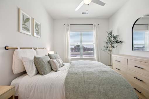 A bedroom with a large bed, a ceiling fan, and a window with blinds. at Park South Apartments, Austin, TX