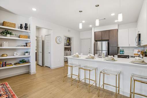 A kitchen with white cabinets and a white island with gold bar stools. at ThreeTwenty at the Vybe Apartments, Kyle, 78640
