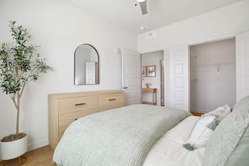 A bedroom with a bed, dresser, mirror, and a plant. at Park South Apartments, Texas