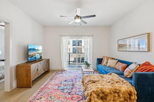 A living room with a blue couch and a wooden cabinet. at ThreeTwenty at the Vybe Apartments, Kyle, TX, 78640