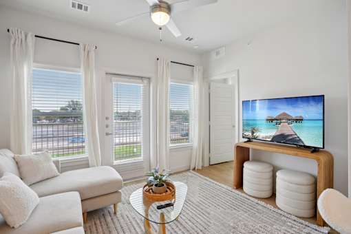 A living room with a television, a couch, a coffee table, and a window with a view of the street. at Park South Apartments, Texas