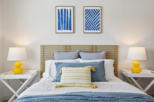 A bed with a blue comforter and yellow pillows is flanked by two white tables with yellow lamps. at Park South Apartments, Texas, 78748