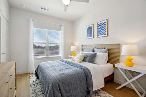 A bedroom with a bed, nightstand, and window. at Park South Apartments, Austin, TX
