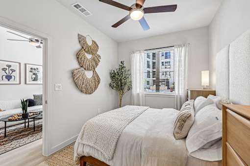 A bedroom with a bed, a ceiling fan, and a wall hanging.