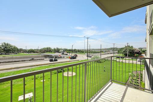 A balcony overlooks a highway with cars and greenery. at Park South Apartments, Austin, Texas
