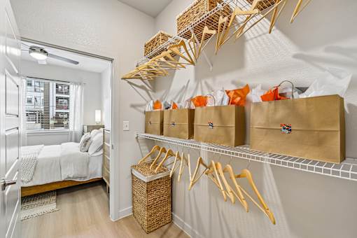 A room with a bed, a window, and a wall-mounted shelf with baskets and bags.
