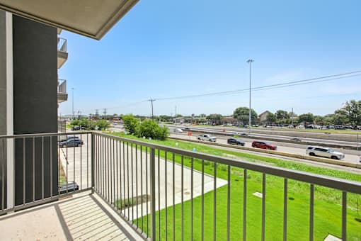 A balcony overlooks a busy highway with cars and greenery. at Park South Apartments, Austin, TX