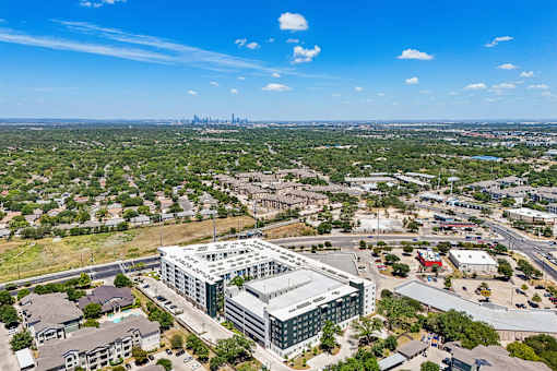 A large building with a green roof is surrounded by smaller buildings and houses.