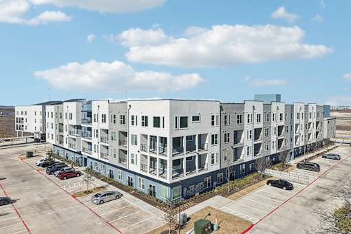 A large white apartment building with a parking lot in front. at ThreeTwenty at the Vybe Apartments, Kyle, TX