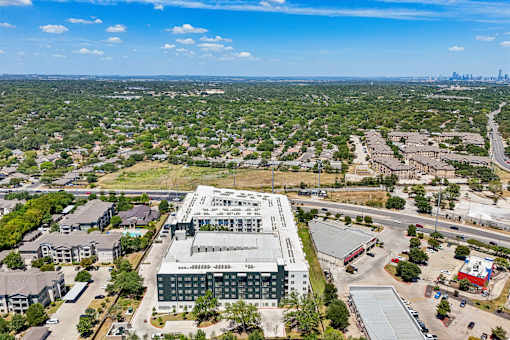 A large building with a green roof is surrounded by trees and other buildings.
