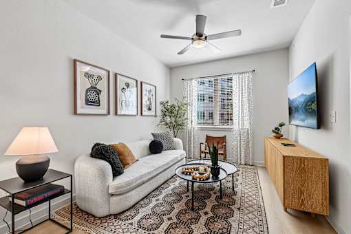 A living room with a white couch, a coffee table, a ceiling fan, and a flat screen TV mounted on the wall.
