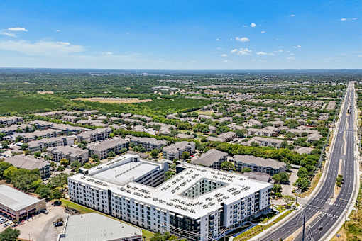 A large building with a glass facade is surrounded by a parking lot and other buildings.