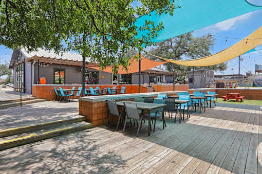 A wooden deck with tables and chairs is surrounded by trees. at Park South Apartments, Austin