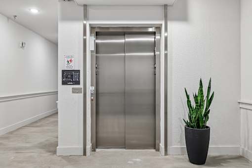 A silver elevator with a sign on the wall and a plant in a pot.